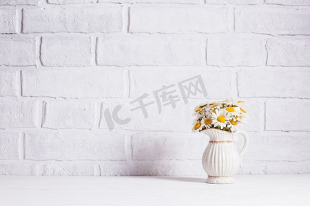 瓶子里的花束摄影照片_家居室内装饰，白色花瓶里有一束雏菊，装饰用的白色瓶子里有放置文字的地方。家居室内装饰