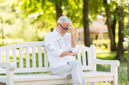 老年、退休与人的概念--一位戴眼镜、深思熟虑的老人坐在夏令营的长椅上。夏令营体贴的老人