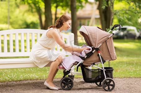 家庭、母性和人的概念-快乐的母亲和孩子在夏季公园的婴儿车里。快乐的母亲推着孩子在夏季公园的婴儿车里