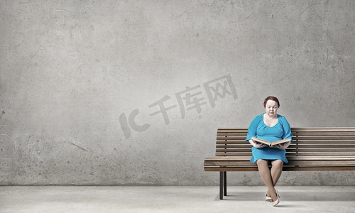 蓝色板凳摄影照片_胖胖的女人。加码女人，手里拿着书，坐在板凳上