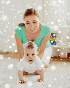家庭、孩子和父母的概念-快乐的微笑的年轻母亲在家中玩雪中的小婴儿。快乐的妈妈在家陪着宝宝玩耍