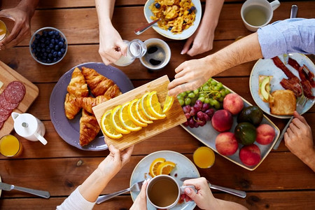 收集食物摄影照片_食物、饮食和家庭概念-一群人吃早餐，在餐桌上分享橙子。在餐桌上吃早餐的一群人