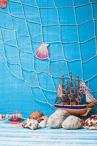 漂亮的海洋构图，蓝色背景上有玩具帆船、贝壳、玻璃瓶和渔网。海上室内装饰