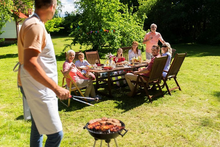 食物、人和家庭时间概念-烹调在烧烤烤架的人肉在夏天游园会。在烧烤烤架的人烹调肉在夏季聚会