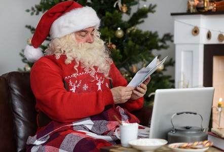 阅读书信摄影照片_圣诞老人在家中圣诞树附近工作。阅读儿童书信