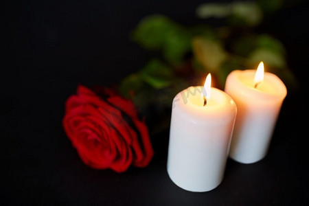 葬礼和哀悼概念-红玫瑰和燃烧的蜡烛在黑色背景上。红玫瑰和燃烧的蜡烛在黑色的背景上