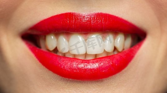 红色口红嘴唇摄影照片_美容、化妆和人的概念--用红色唇膏特写微笑的女人嘴唇或嘴巴。涂着红色口红的微笑女子的嘴唇或嘴巴