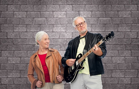 音乐、年龄和人的概念快乐的老年夫妇在砖墙背景下使用电吉他。拥有电吉他的快乐高年级夫妇