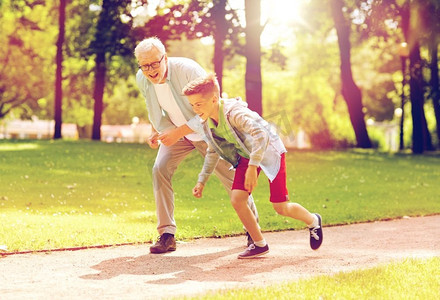 儿童赛车摄影照片_家庭、世代和人的概念-快乐的祖父和孙子在夏季公园赛车。祖父和孙子在夏季公园赛车