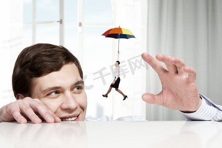 年轻男子从桌下看女商人撑着伞飞。他是个大老板