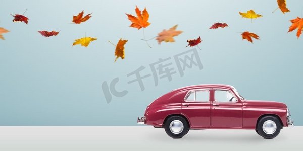 秋季背景简约摄影照片_简约的秋季车。极简主义蓝色背景下落叶的秋红玩具车