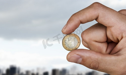 手指间夹着五欧元硬币。近距离观察男性用手指握手的欧元硬币