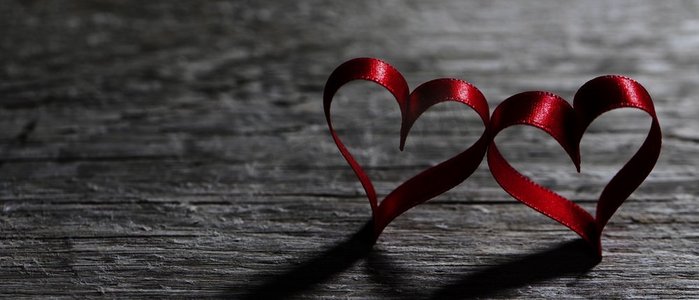 木头上有两颗心形的丝带。木质背景上的两个红丝带心形，情人节概念