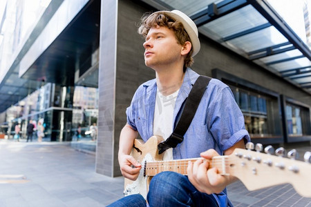 弹吉他的人摄影照片_城市里弹吉他的年轻音乐家。城市里拿着吉他的年轻音乐家的肖像