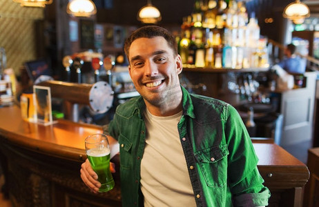 人，休闲和圣帕特里克节的概念-在酒吧或酒吧喝绿啤酒的快乐年轻人。在酒吧或酒吧喝绿啤酒的男人