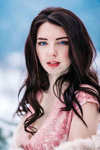 在冬日群山的背景下，一个棕色头发，蓝色眼睛，穿着粉色连衣裙的女孩