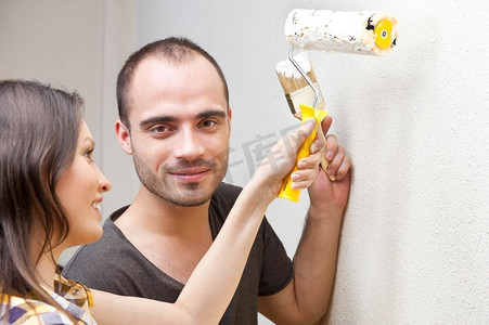 粉刷滚筒摄影照片_一对年轻夫妇用滚筒粉刷墙壁，一起在家修缮