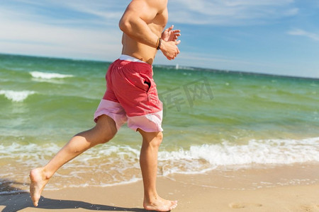 健身，运动，人和健康的生活方式理念-快乐的年轻人沿着夏天的海滩跑步。快乐的男人沿着夏日海滩跑步