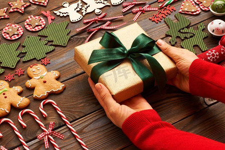 一名女子在木质背景上拿着圣诞礼物，上面有自制的姜饼饼干和手工装饰