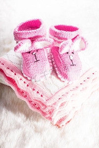 婴儿毛毯摄影照片_为小女孩编织的粉色婴儿靴子和毯子。针织婴儿靴