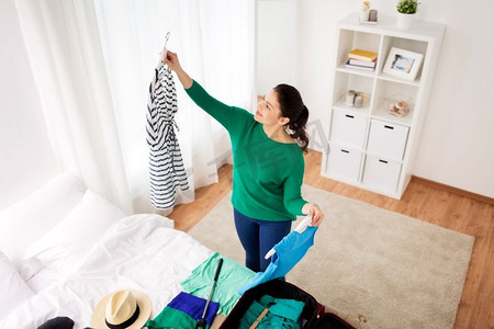 旅游，人和行李的概念-快乐的年轻女子在家里或酒店房间里收拾旅行包。在家里或酒店房间里收拾旅行包的女人