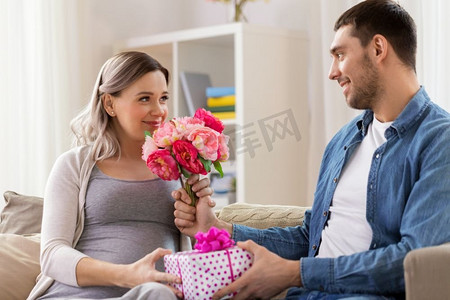 送花的男人摄影照片_节日、怀孕和问候的概念-快乐的男人在家给怀孕的女人送花。男子在家中向孕妇献花