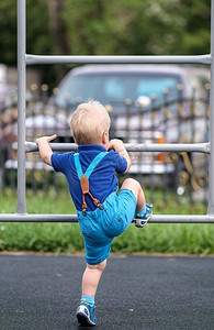 攀岩男孩摄影照片_穿着短裤和吊带的蹒跚学步的孩子在户外的肖像。一岁的男婴在操场上