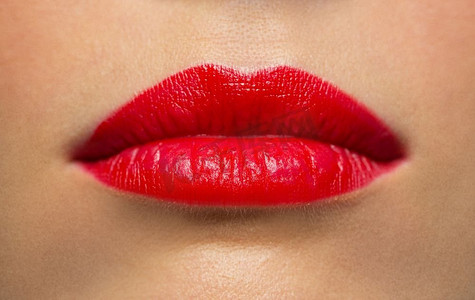 红色口红嘴唇摄影照片_美容、化妆和人的概念--用红色口红将女人的嘴唇或嘴巴特写。涂着红色口红的女人的嘴唇或嘴巴