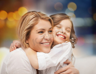 家庭和母亲的概念-快乐的母亲和小女儿拥抱在节日的灯光背景。幸福的母亲和小女儿拥抱
