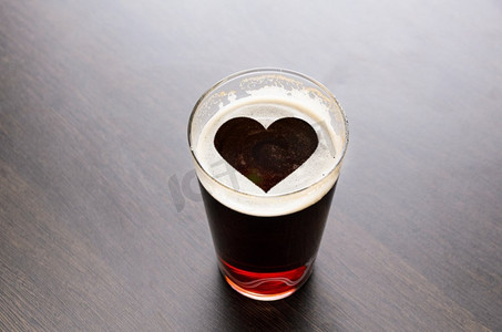 气泡剪影摄影照片_黑色桌子上的啤酒玻璃泡沫上的心形剪影，从上面看。