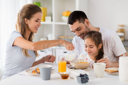 孩子和母亲摄影照片_家庭、饮食和人的概念-幸福的父母和女儿在家里吃早餐。幸福的一家人在家里吃早餐