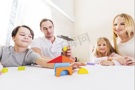 有孩子的家庭在盖房子。一家四口带着孩子建造玩具积木房子，房地产概念