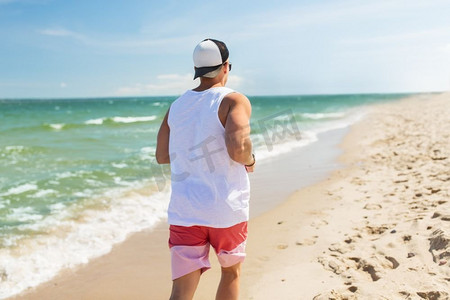 海滩跑步摄影照片_健身，运动，人和健康的生活方式理念-快乐的年轻人沿着夏天的海滩跑步。快乐的男人沿着夏日海滩跑步