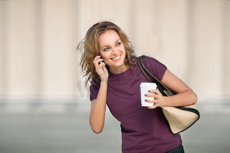一个漂亮的女人拿着电话，端着一杯外卖咖啡。