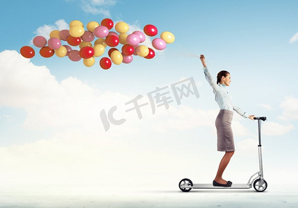 骑滑板车的年轻女子。年轻女子骑着摩托车，手里拿着一串气球