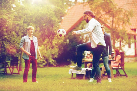 休闲，假期，人和运动的概念-快乐的朋友在夏日游园会上踢足球。快乐的朋友在夏日花园踢足球