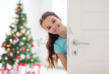 家里的门摄影照片_童年，快乐和人的概念--在家里的门后微笑的美丽的女孩。快乐微笑的漂亮女孩在家里的门后