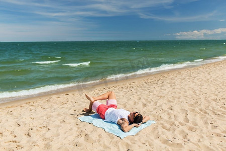 暑假和人们的概念-快乐微笑的年轻人在沙滩毛巾上日光浴。快乐微笑的年轻人在沙滩毛巾上晒日光浴