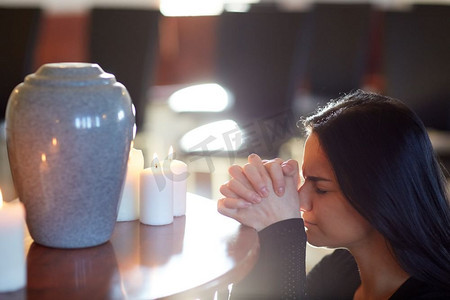 人和哀悼的概念-悲伤的女人在教堂的葬礼上用骨灰盒和蜡烛祈祷。悲伤的女人带着骨灰盒在教堂祈祷