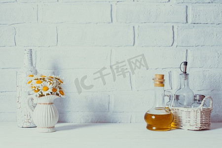 家居室内装饰，白色花瓶里的雏菊花束，装饰性的白色瓶子和篮子里的玻璃瓶油瓶。家居室内装饰