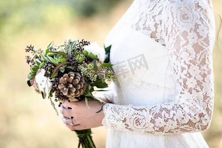新娘的花束从锥和棉花关闭了在新娘的手中花边礼服森林背景