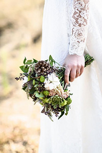 花边摄影照片_新娘和S手中的花束由球果和棉花制成，紧贴在新娘手中的花边礼服林立的背景