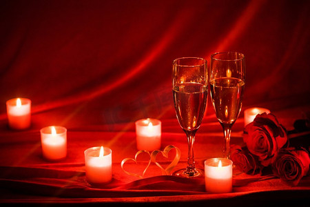红丝绸摄影照片_香槟和蜡烛。情人节庆祝活动，红丝绸上的香槟、蜡烛、玫瑰和红心
