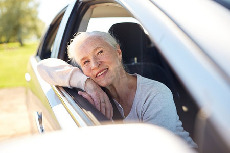 公路旅行，旅行和老人概念-快乐的老年妇女开着开着车窗的车。快乐老太太开着开着车窗的车