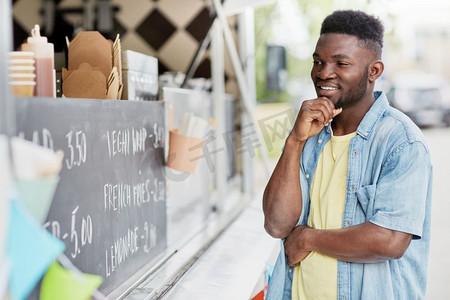 食品外卖车摄影照片_街头打折和人物概念-男性顾客看着美食车的广告牌。在美食车前看广告牌的男性顾客