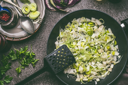 在黑色煎锅里切成片的韭菜，背景是乡村厨房的桌子，俯视。健康素食烹饪与饮食，饮食理念