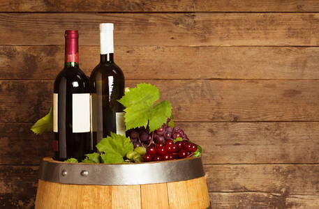橡木桶上的一瓶瓶葡萄酒覆盖着破旧的木质背景。几瓶葡萄酒