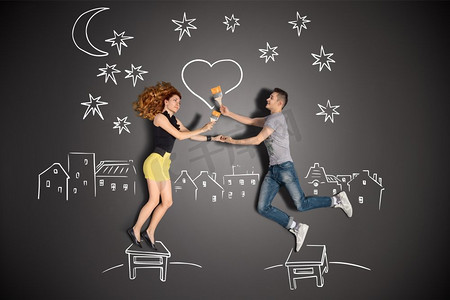 一对笔画摄影照片_一对浪漫夫妇的愉快的情人节爱情故事概念站在凳子和画一个心脏在夜空反对粉笔画背景.