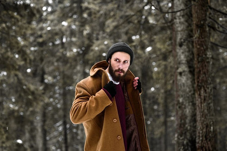 戴手套冬天摄影照片_冬天森林里的人很冷，穿着棕色的外套，戴着手套