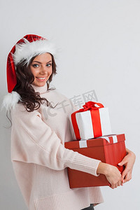 礼物一堆摄影照片_一堆礼物的女人。在圣诞老人帽子的快乐的女人与圣诞节礼物堆